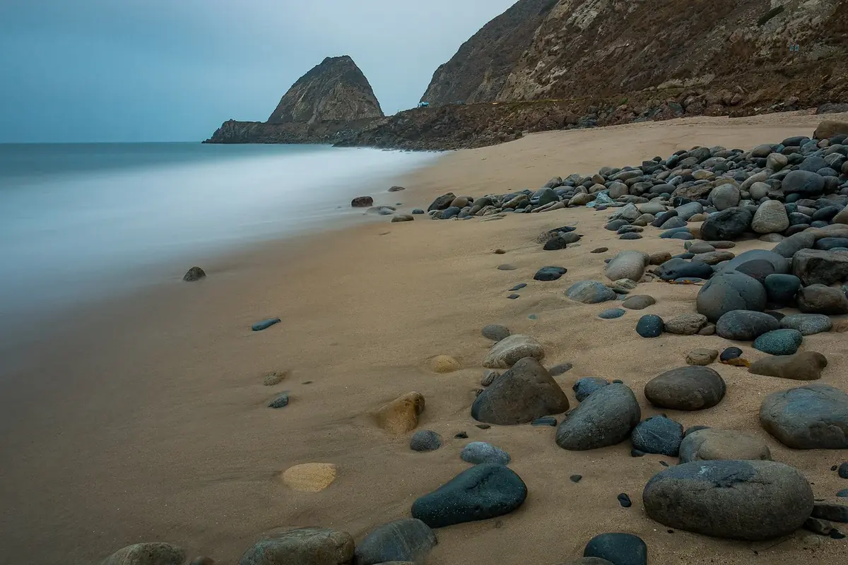 a rocky beach at low tide with a headland and calm ocean behind it
