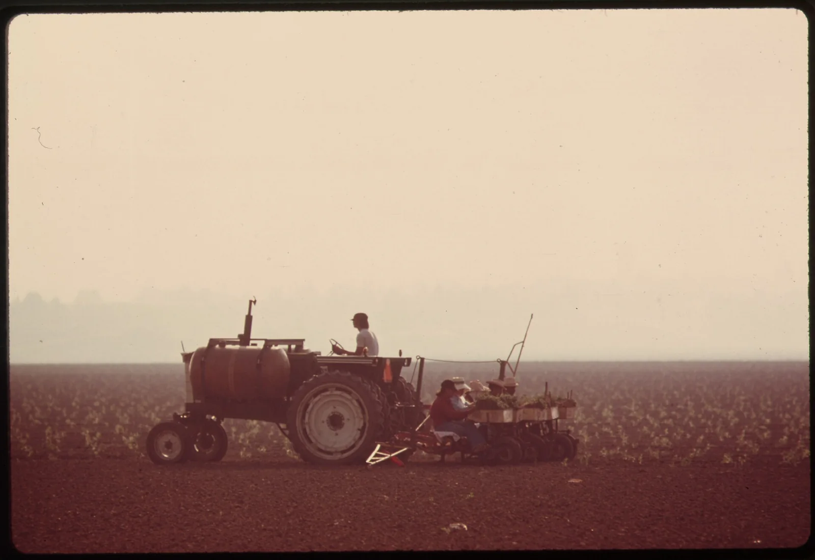 a farmer on a tractor crossing a flat field in haze